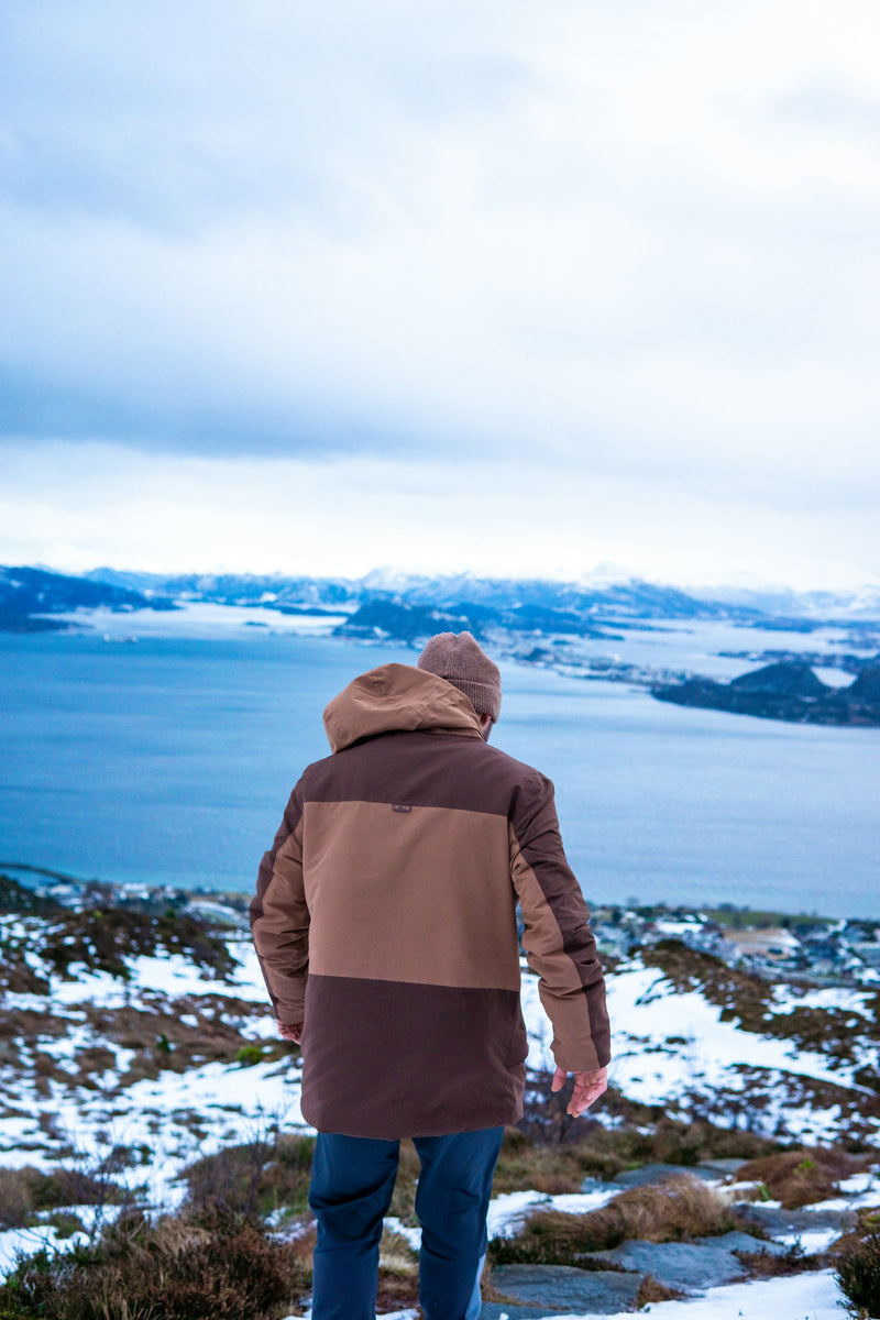 Persona con parka impermeable frente a un fiordo nevado