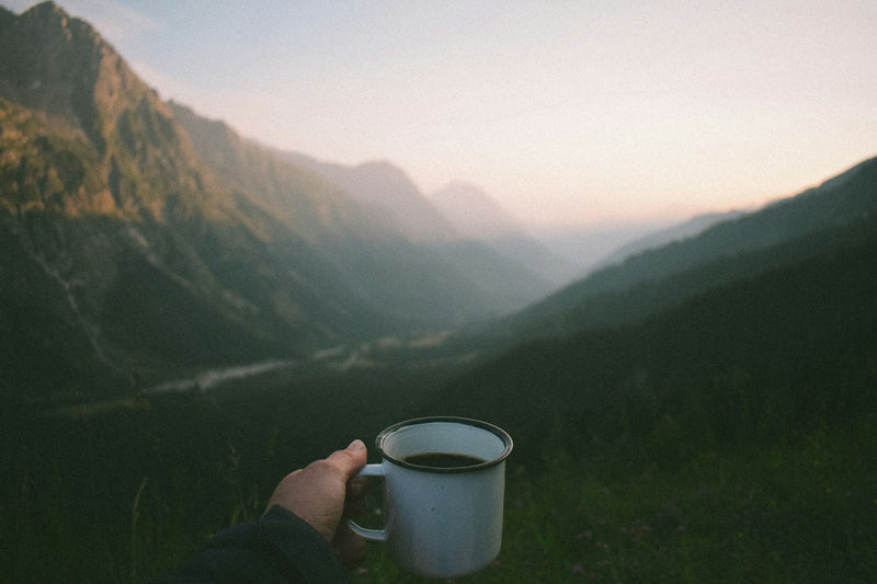 Taza de café caliente frente a un valle de montaña al atardecer